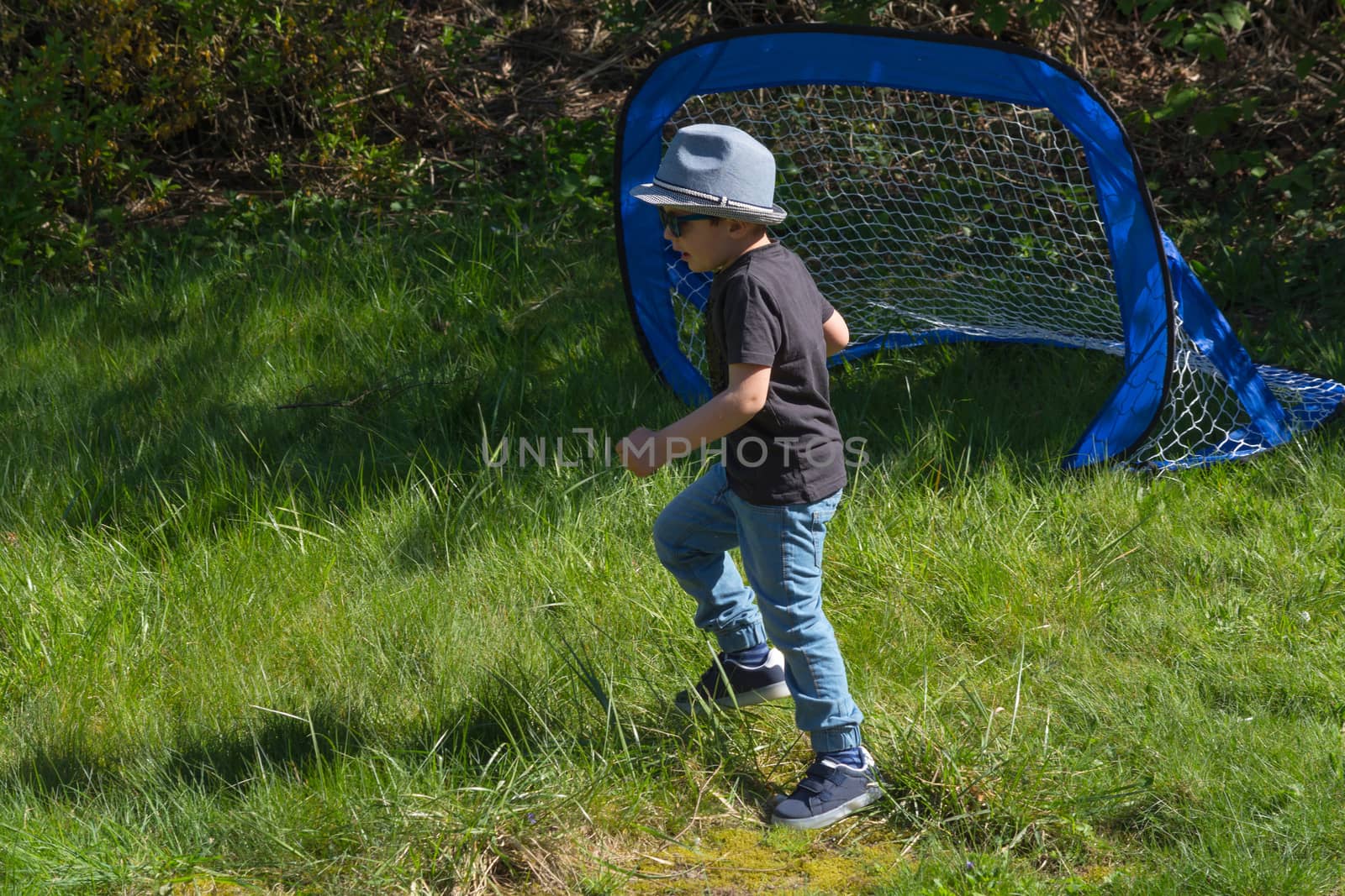 Little boy with hat and sunglasses while playing football in a garden