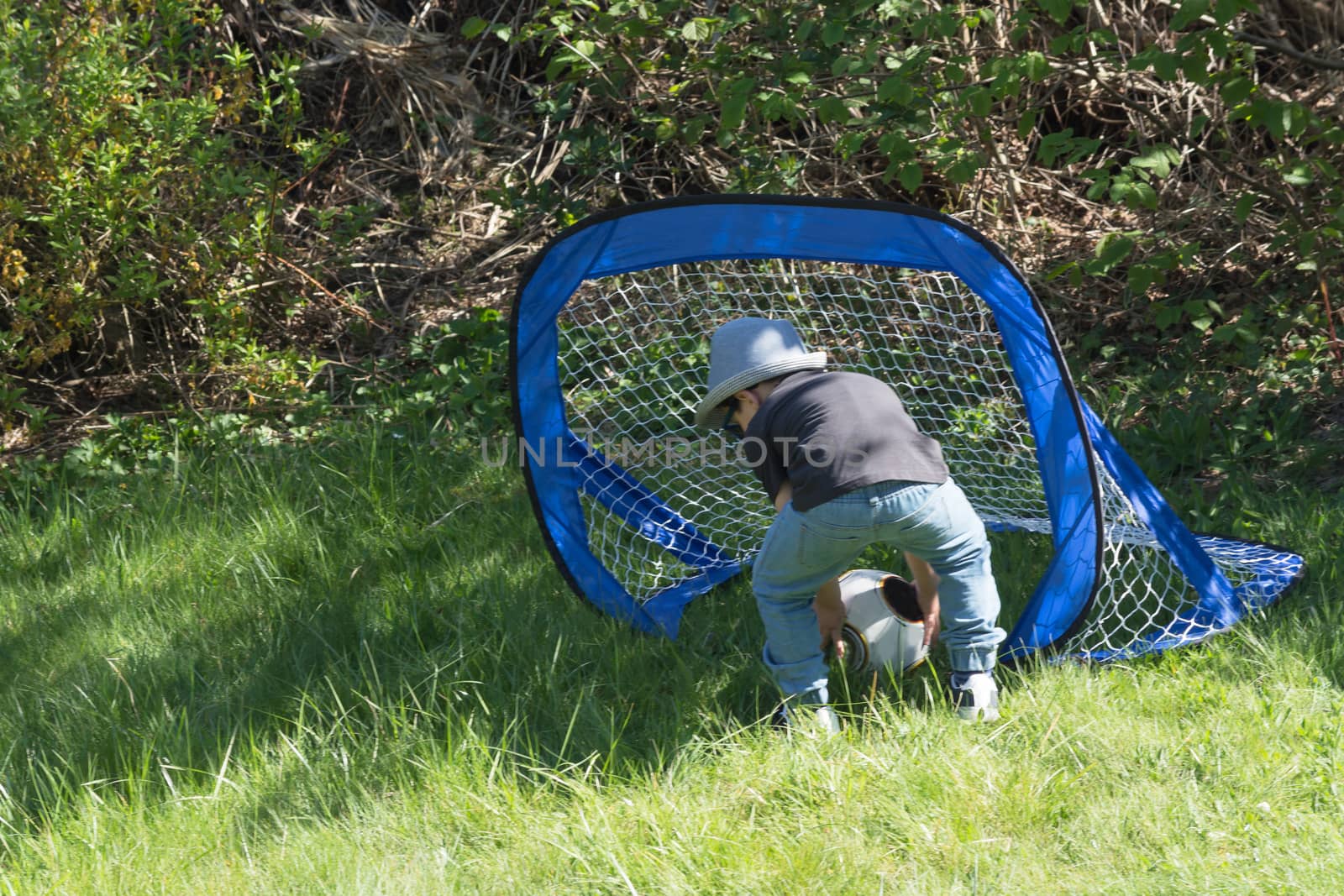 Little boy with hat and sunglasses while playing football in a garden