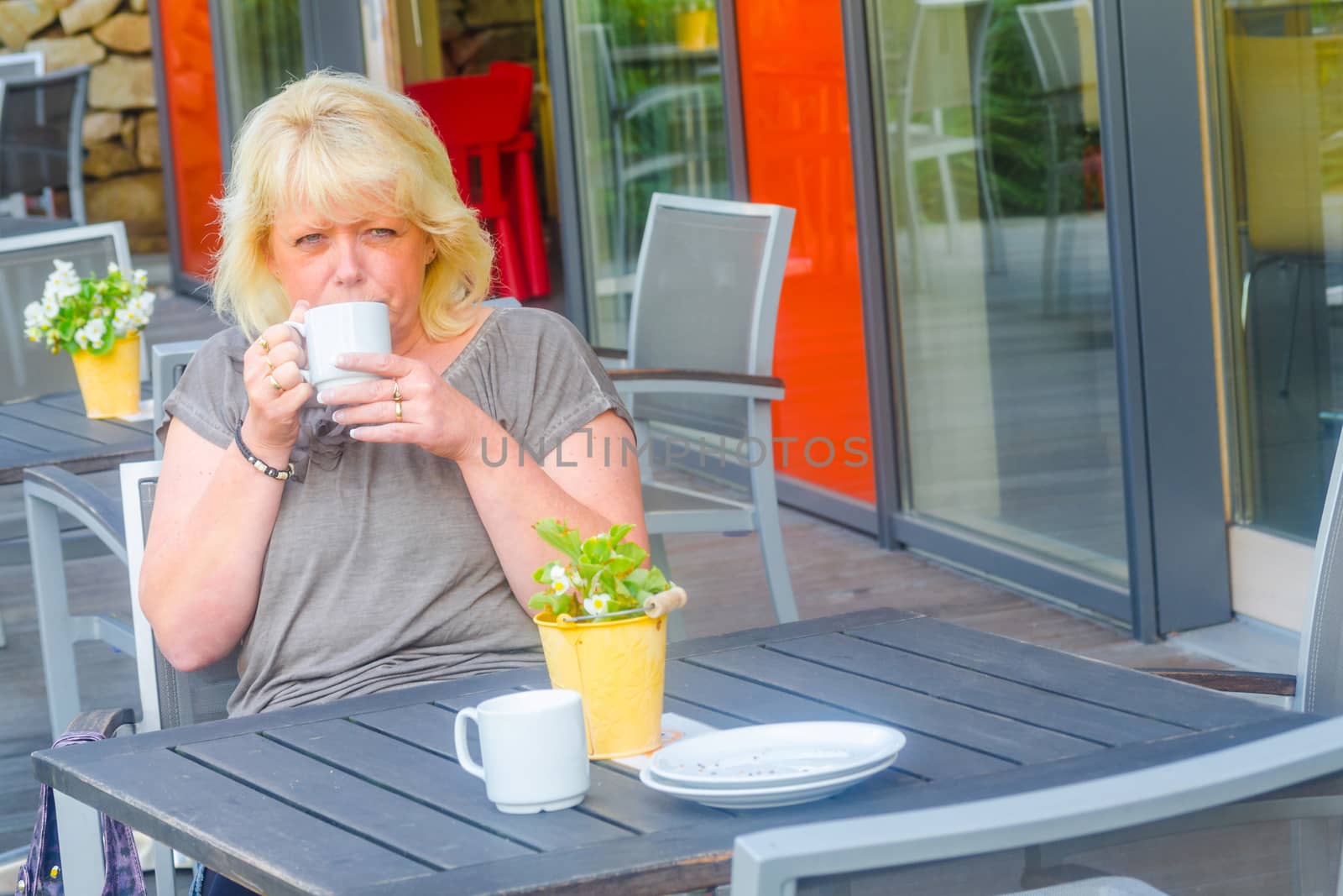 Blond woman enjoys a coffee in a sidewalk cafe.