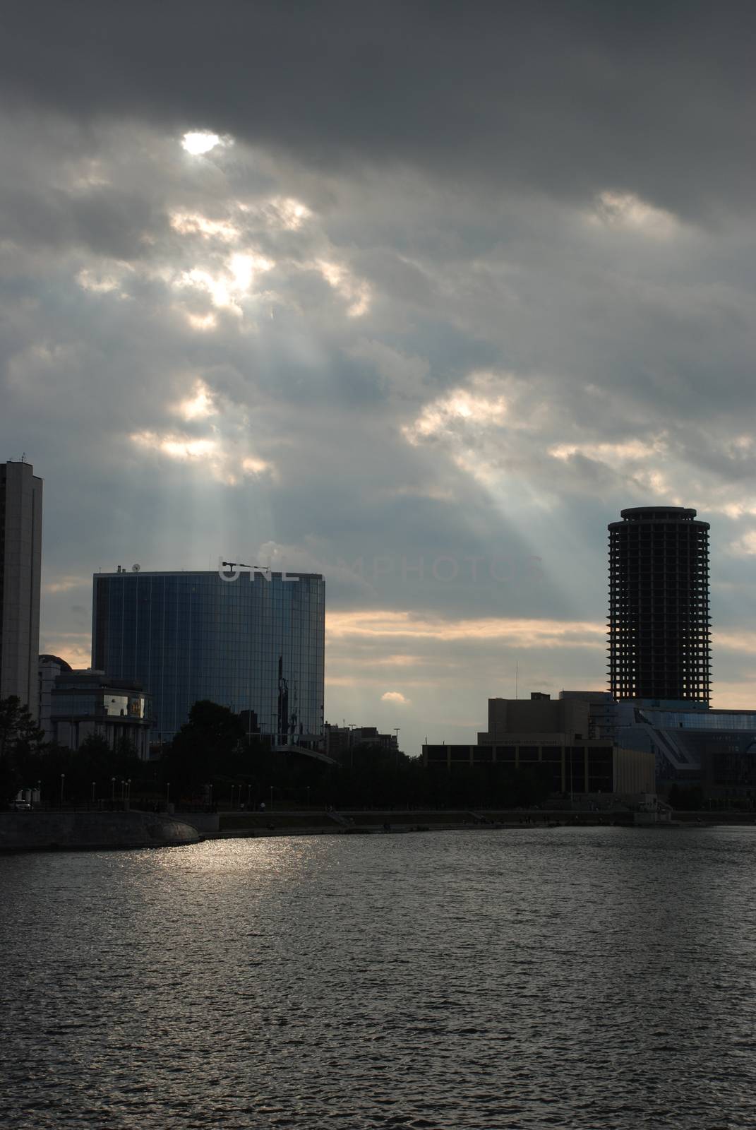 Rays of the sun coming through clouds over the buildings near the river