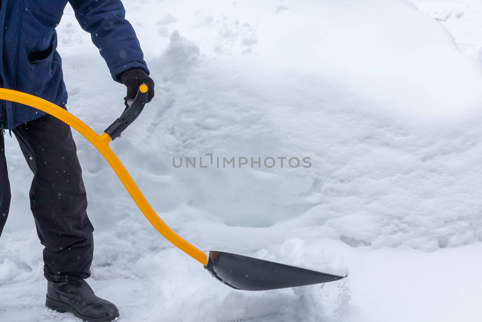 A man cleans snow in the yard with a shovel after a heavy snowfall.