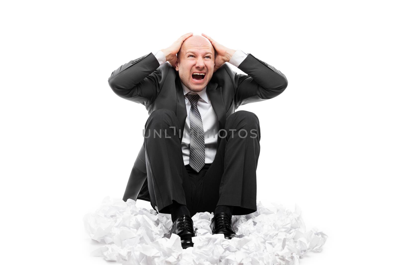 Business problems and failure at work concept - loud shouting or screaming tired stressed businessman hands covering ears for silence sitting floor on crumpled torn paper document heap white isolated