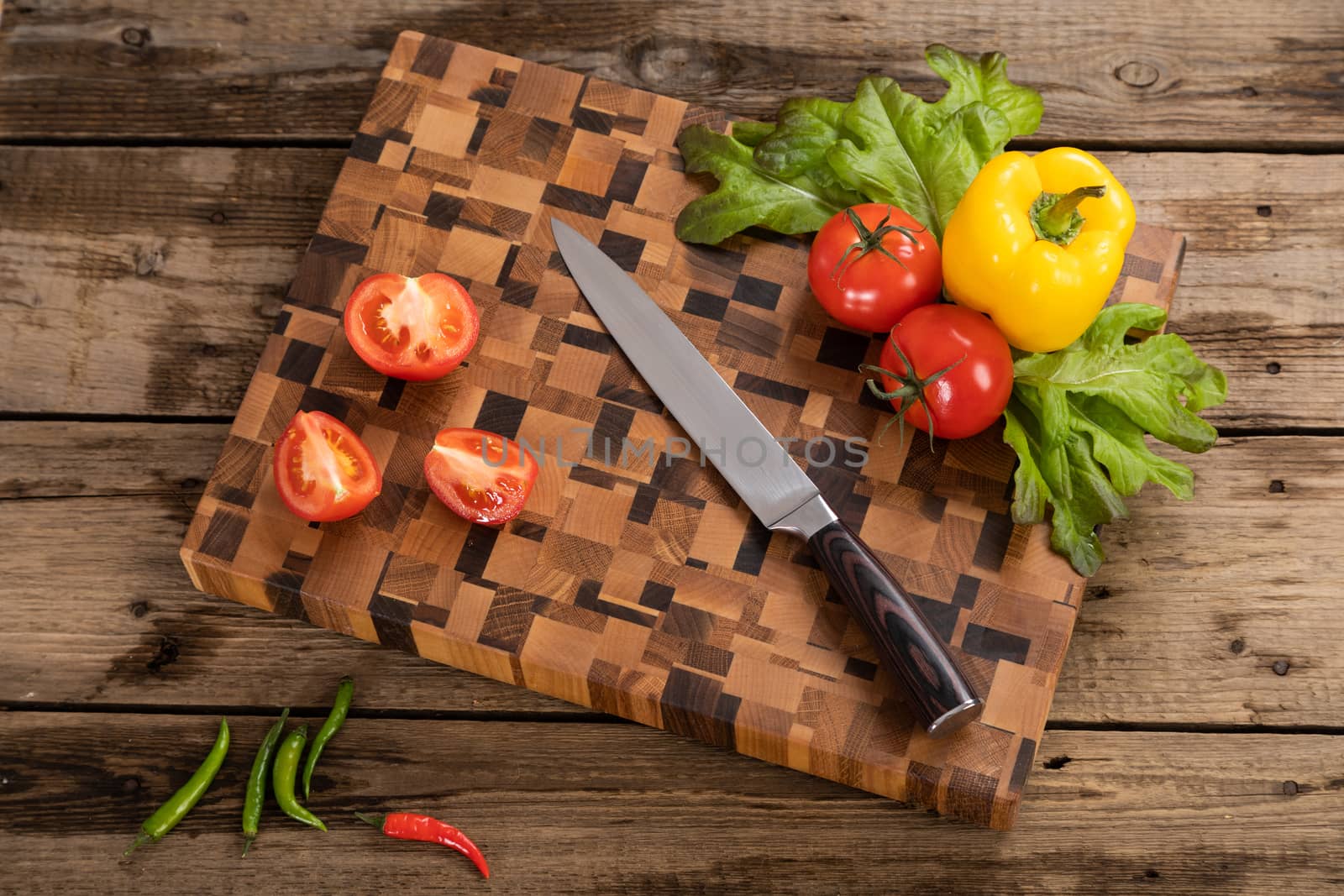 Red, ripe, bright tomatoes and peppers lie on a wooden cutting board near the kitchen knife. by sveter