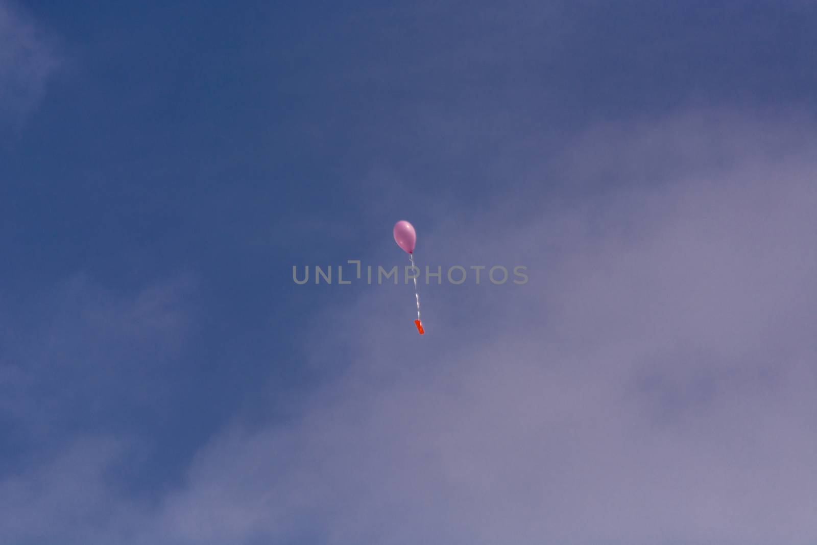 Pink balloon with ribbon and greeting card in front of blue sky