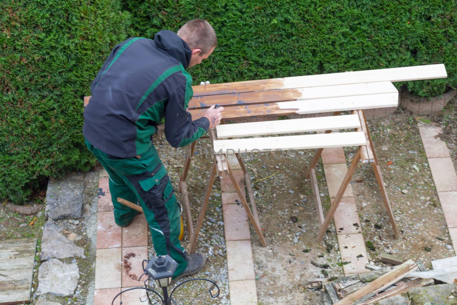 Man strokes protective paint on wooden garden furniture.  by JFsPic