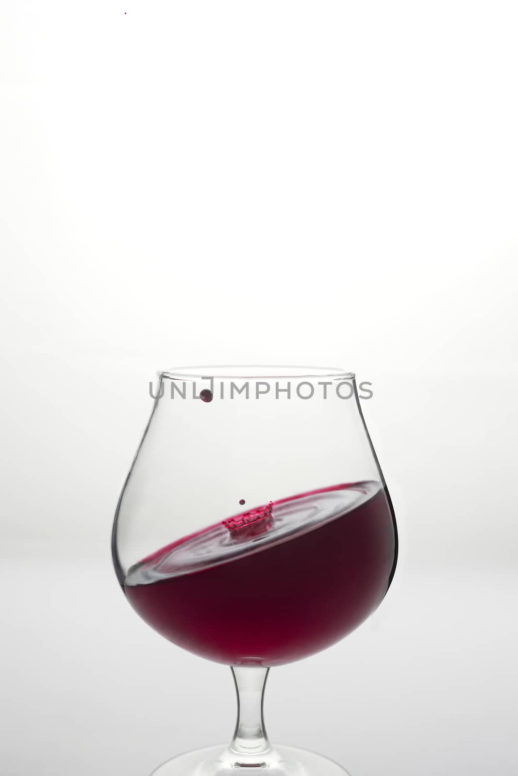 Creative wine glass with inclined level of wine and wine drop above it on white background. Wine is not subject to gravity. Conceptual photo for sommelier and gourmet. 