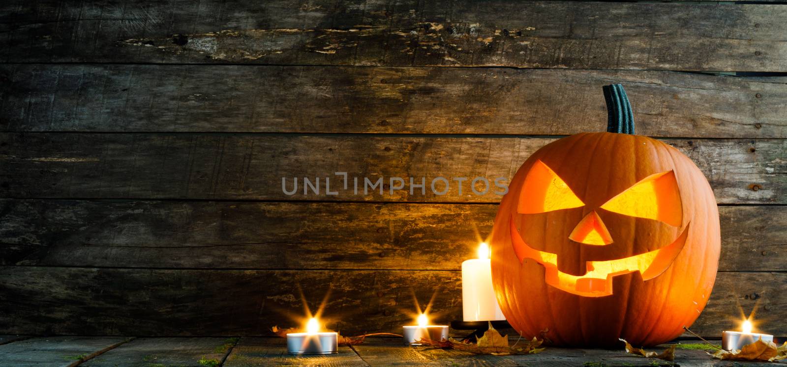 Halloween pumpkin head jack lantern and candles on wooden background