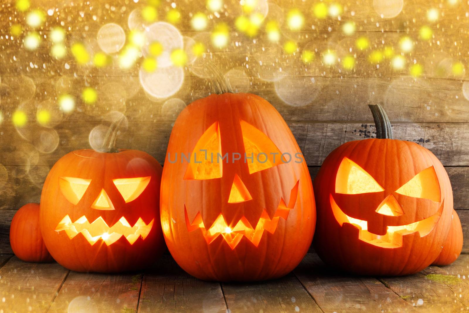 Three halloween pumpkins in magic golden bokeh lights around