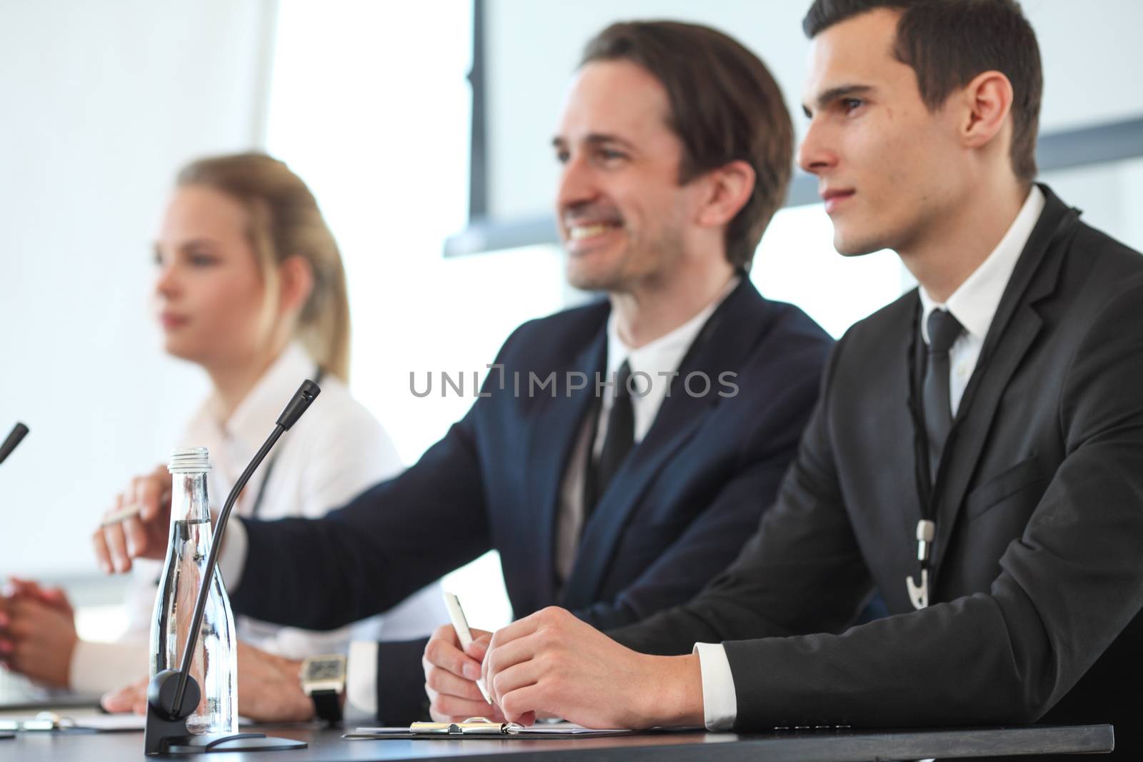 Group of speakers at business meeting at the table with microphones