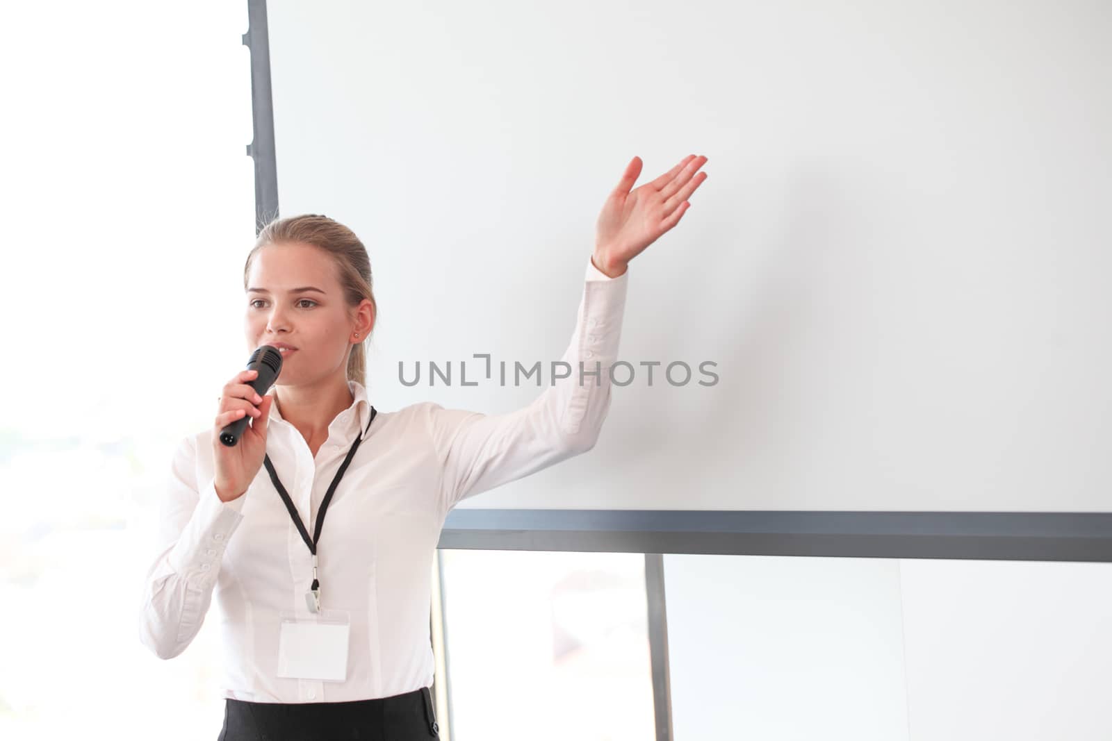Business woman speaker or teacher points at a whitespace screen copy space background