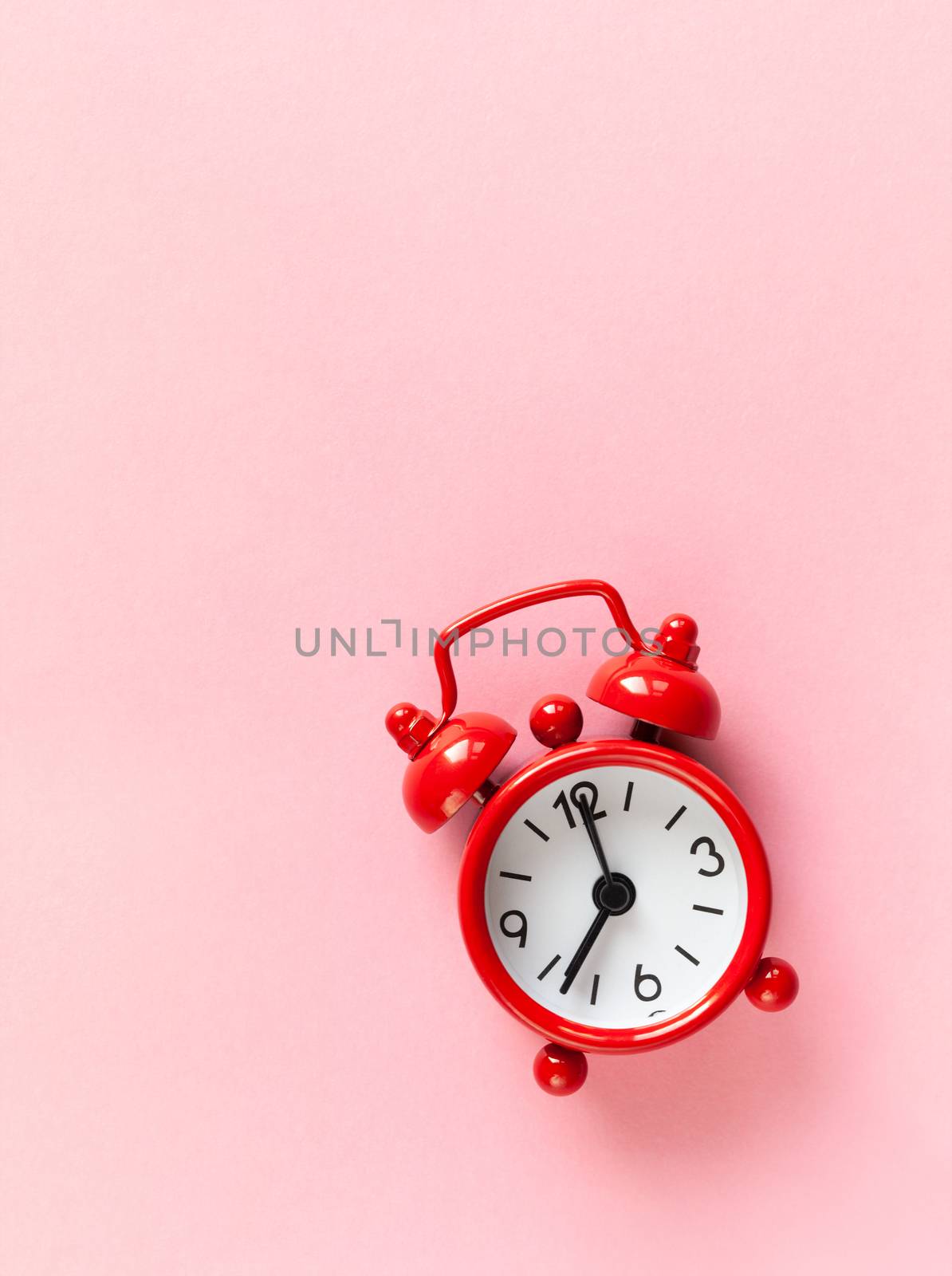 Red small alarm clock on pastel pink background with copy space, flat lay, macro. Minimal style. Time management concept. Vertical.