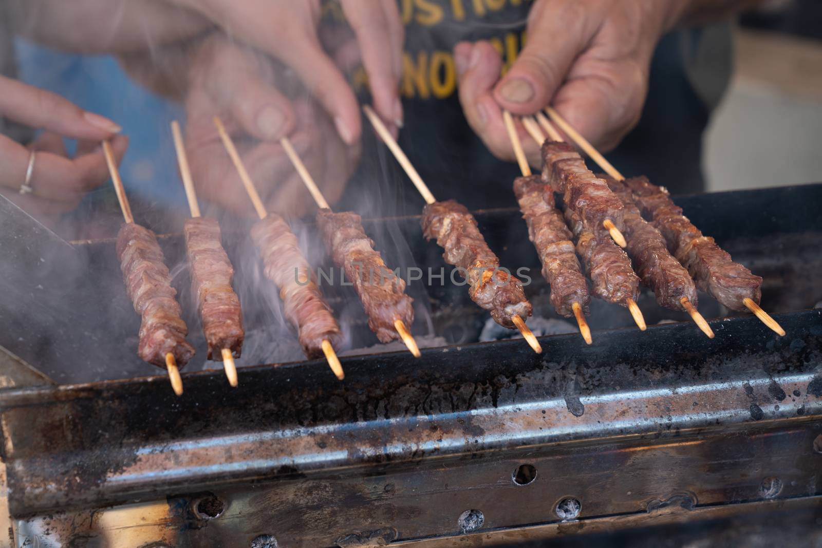 Man cooking marinated meat, Pork meat grilling on wooden skewer, outdoor grill with smoke coming up from the fire below. close up