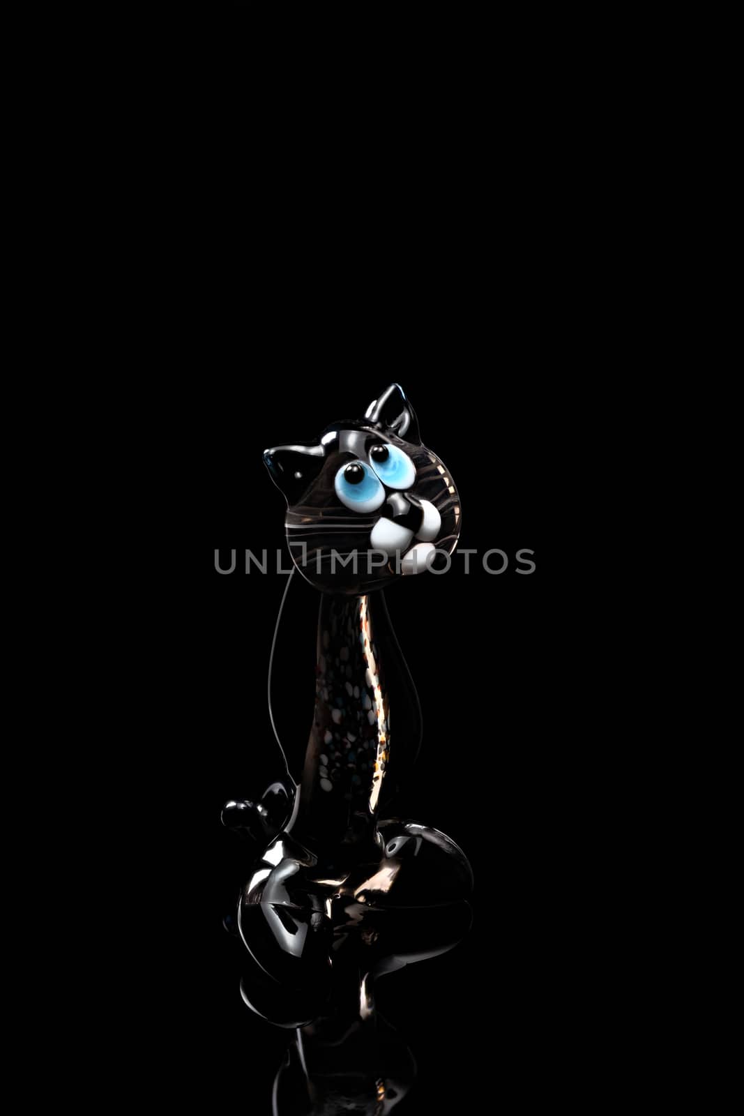 A fugurine of transparent black cat isolated on black background. Stock photo of glass handmade figurine.