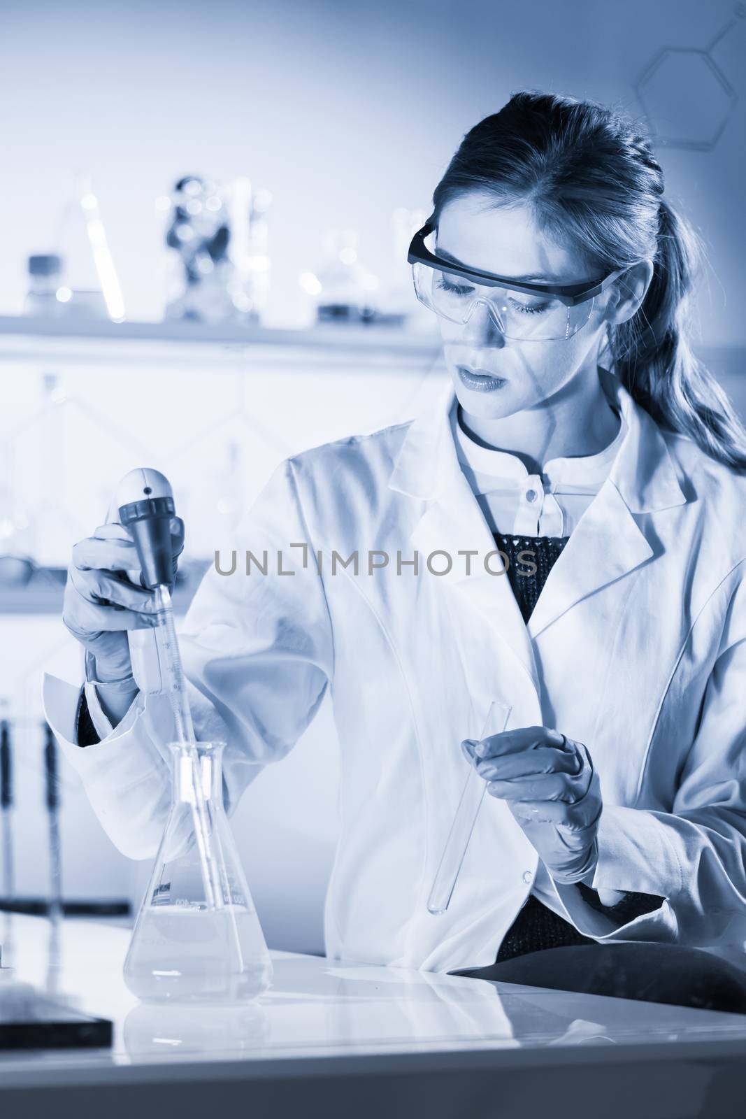 Life scientists researching in laboratory. Focused female life science professional pipetting solution into the glass cuvette. Healthcare and biotechnology concept. Blue toned image.