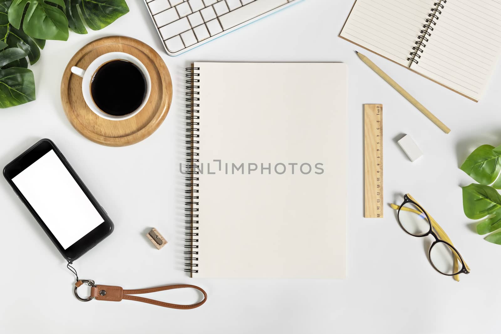 Flat lay of white office desk table with blank notebook, supplies and coffee cup. Top view with copy space.