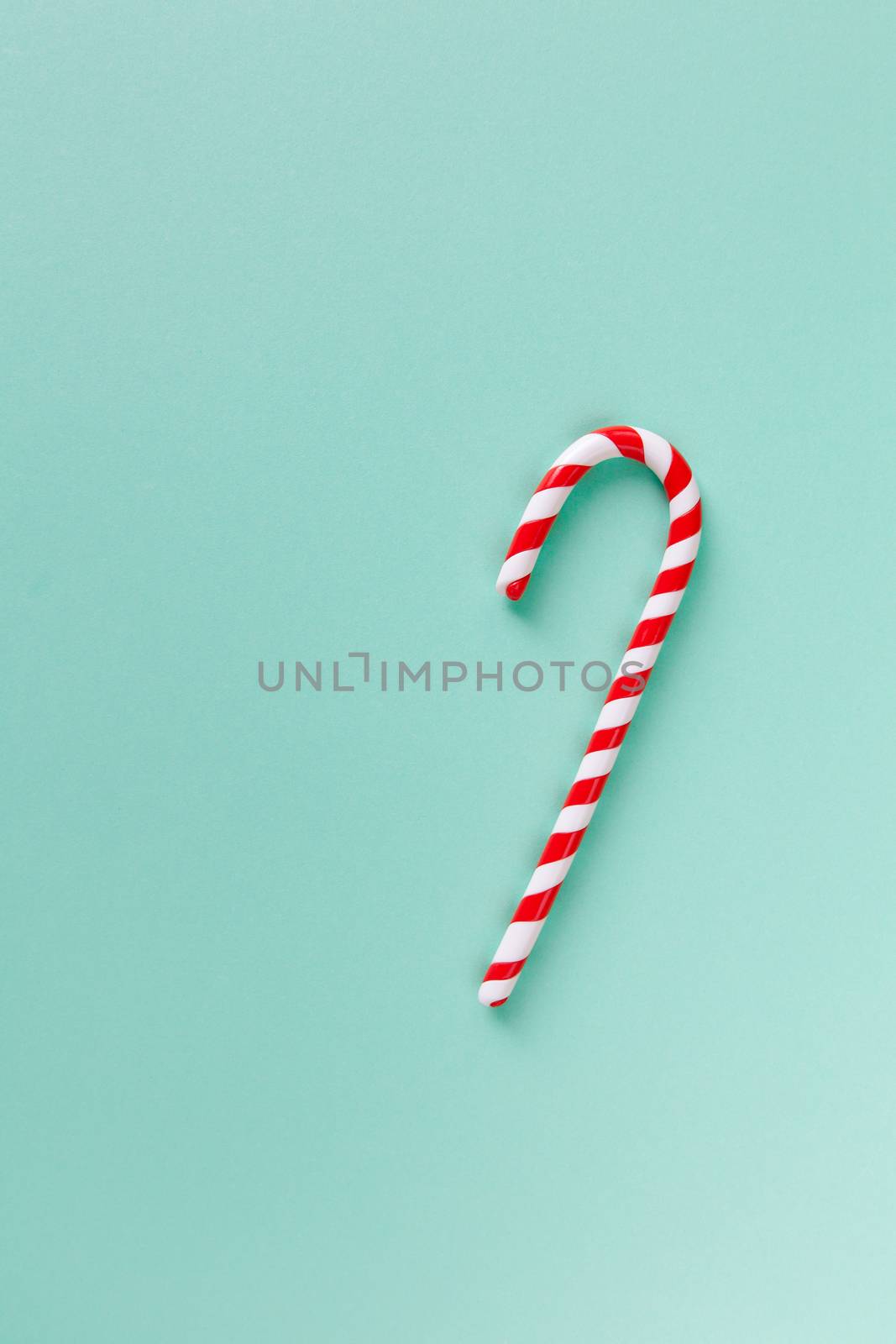 Christmas peppermint candy cane on pastel turquoise background. Festive minimal style flat lay. Mockup with copy space for greeting card, invitation, social media. Vertical.