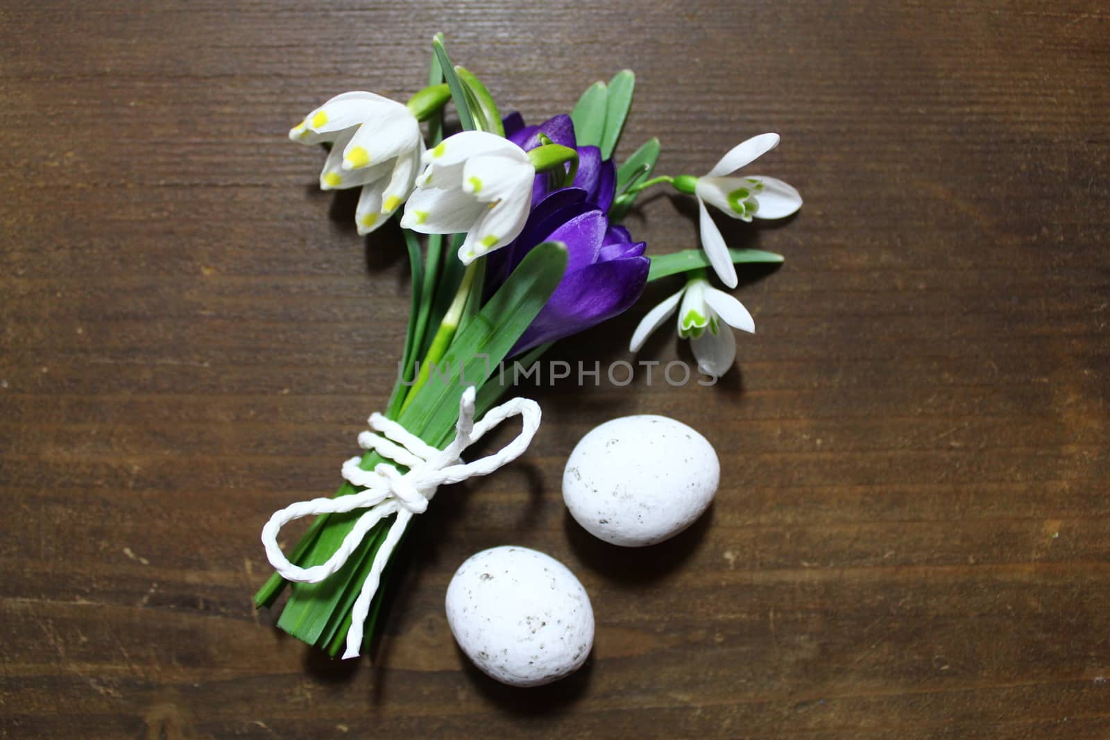 The picture shows early flowering plants with eastereggs on a brown table.