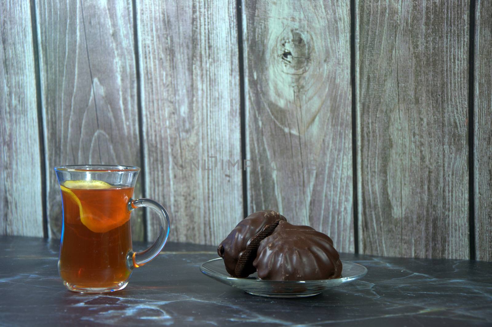 A cup of tea with lemon and a saucer with two chocolate marshmallows. Close-up.