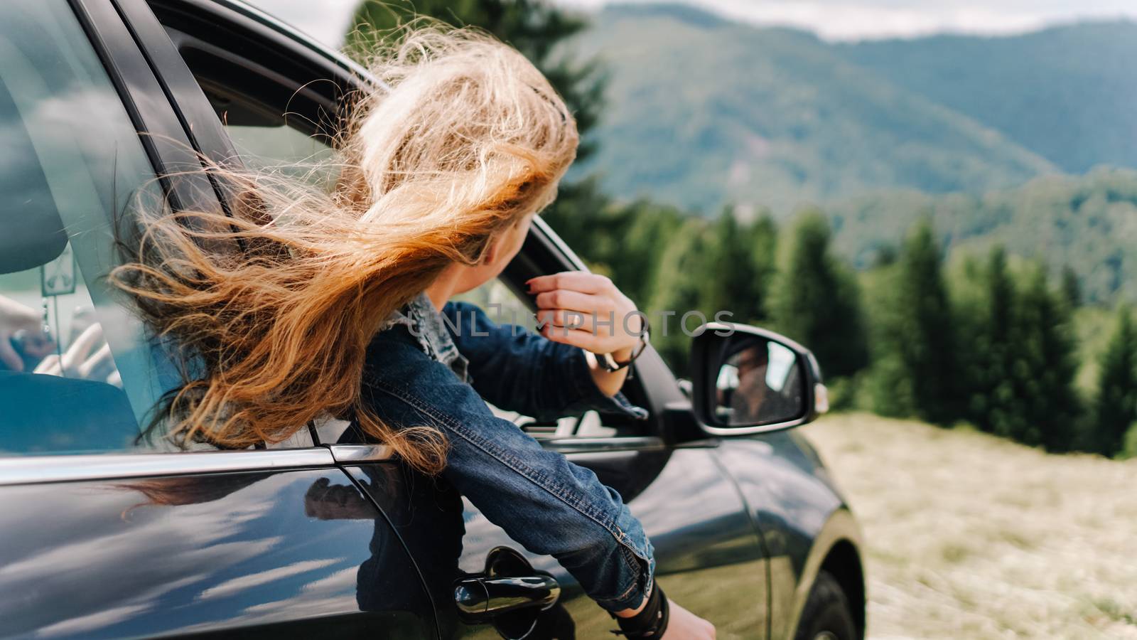 Happy woman travels by car in the mountains. Summer vacation concept. Woman out the window enjoying mountain view
