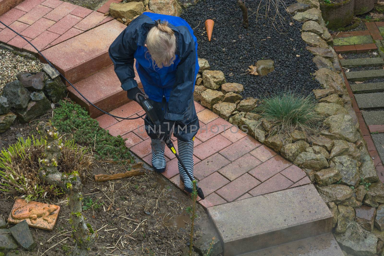 Woman cleans stone slabs with a pressure washer