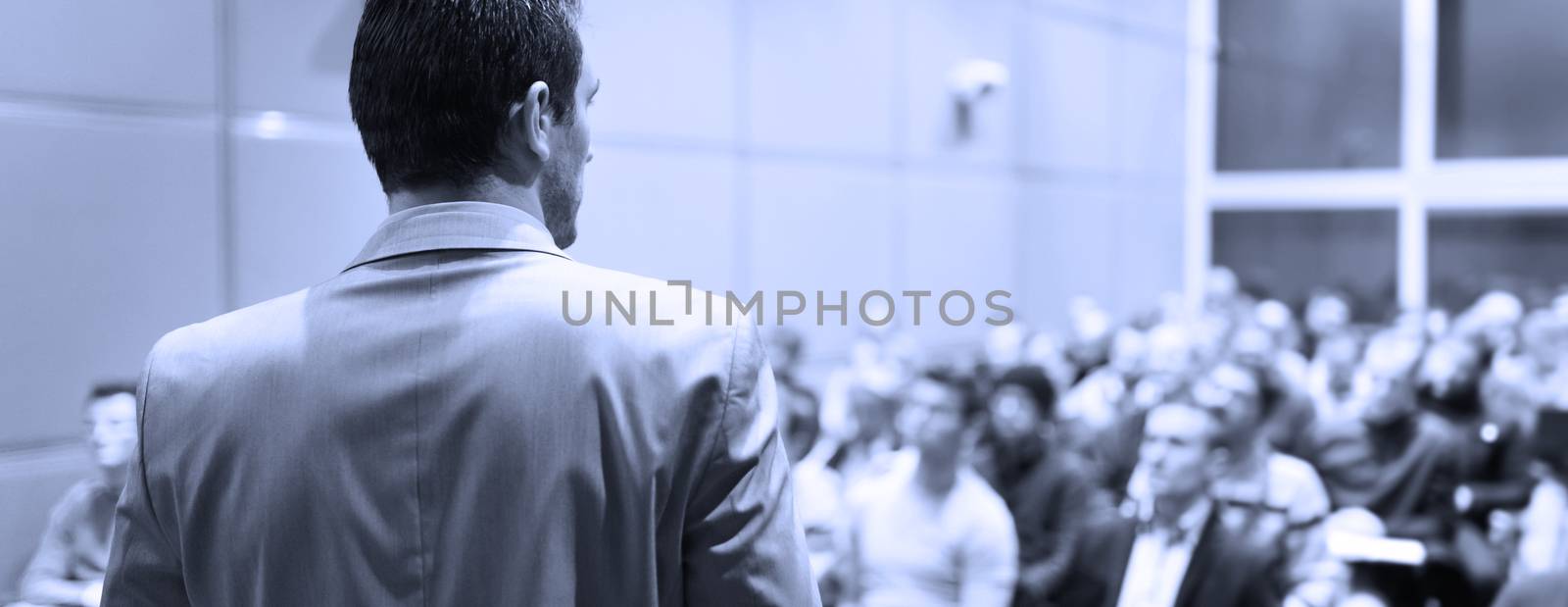 Speaker at Business Conference with Public Presentations. Audience at the conference hall. Business and Entrepreneurship concept. Background blur. Shallow depth of field. Blue toned.
