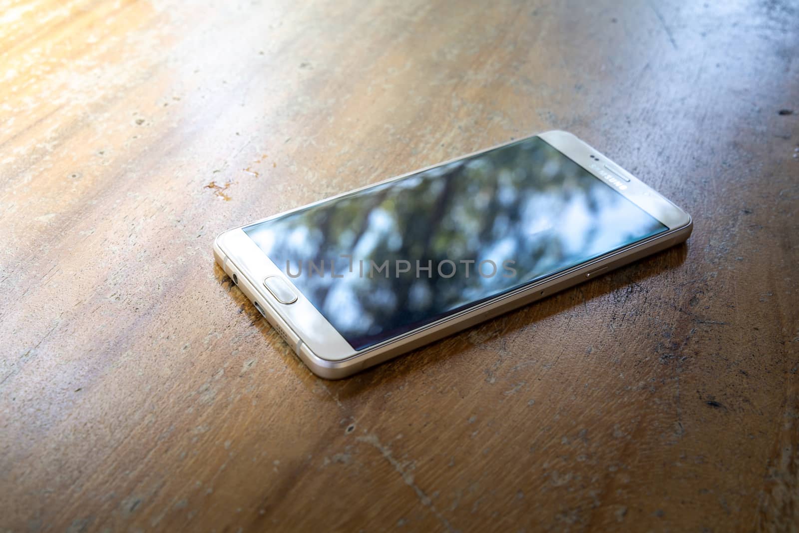 The smart phone is on a wooden table on a bright sunny day.