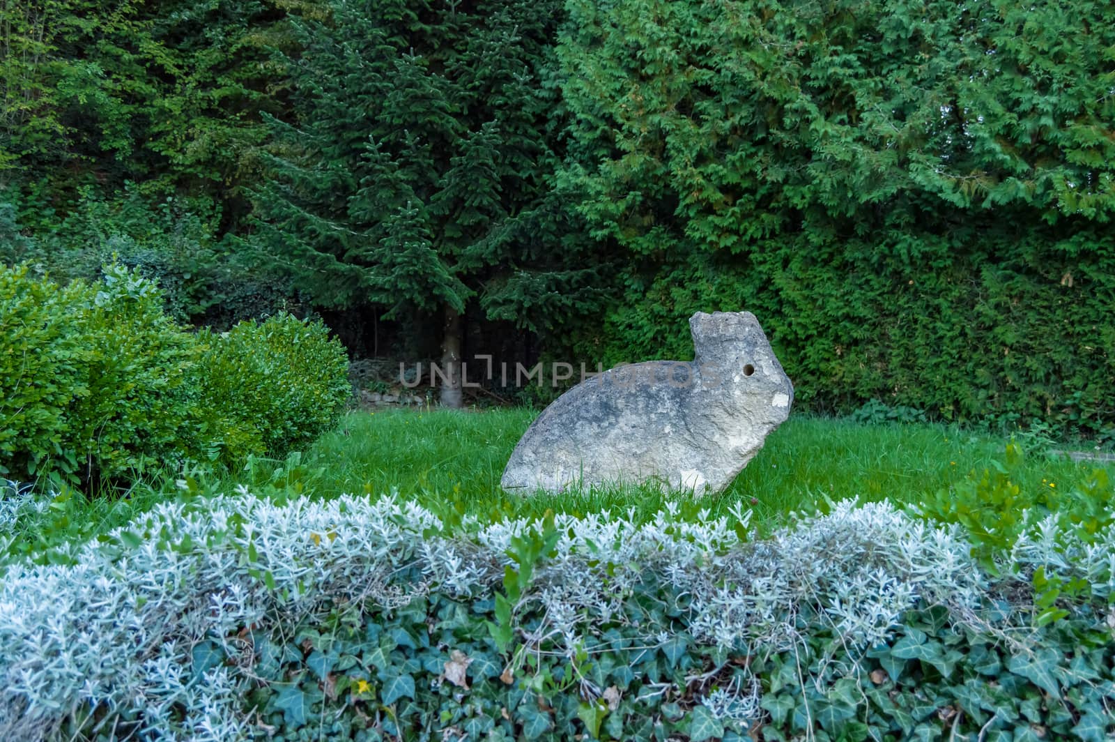 Sculpture of a stone rabbit on a lawn next to a bush in the city of Meix in front of Virton in Belgium