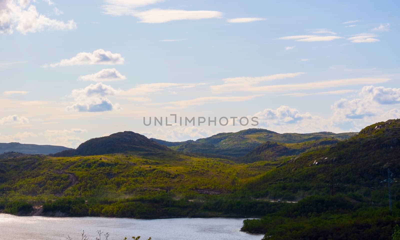 Green hills under a low, deep Northern sky and peacefull lake. These places in the Murmansk region are not far from Teriberka. Clouds fly over the trees and hills. Quiet and peaceful landscape