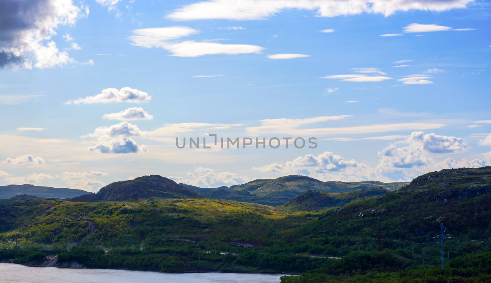 Blue sky over the hills in the Murmansk region. The low Northern sky breaks through the rays of the sun, reflected from the trees and bushes. Murmansk region, near Teriberka. Russia
