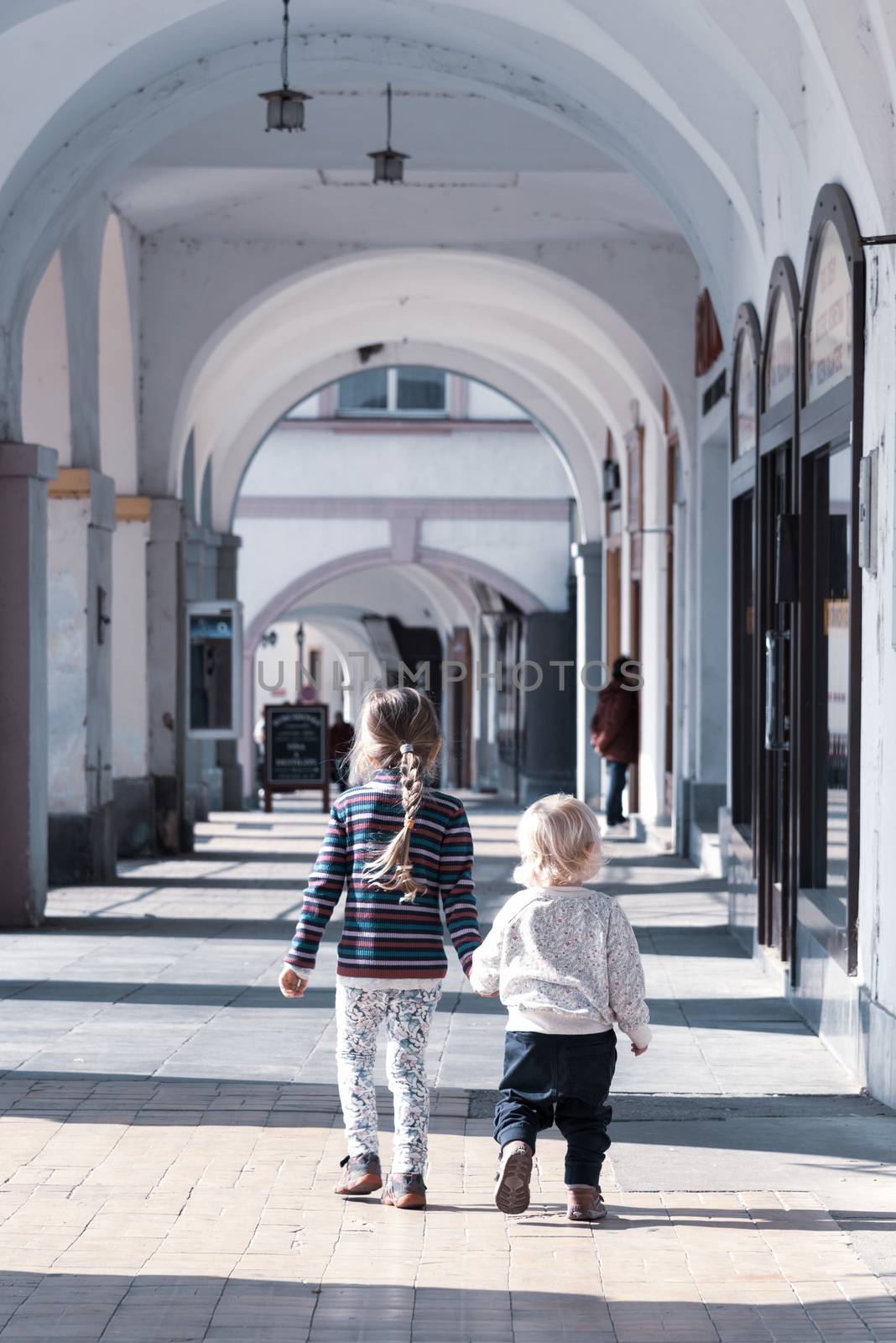 Two young children walk together hand in hand in the old town arcade street. Family love and friendship theme by pyty