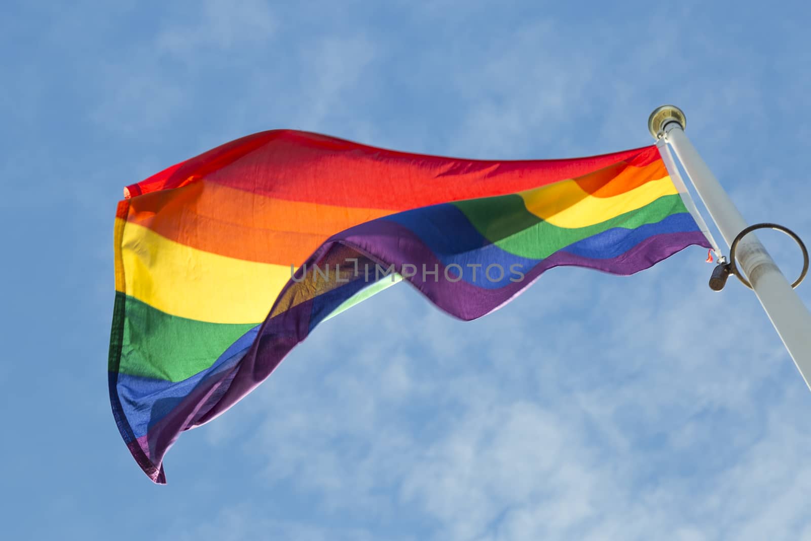 Rainbow Flag waving in the wind with a partly cloudy sky.