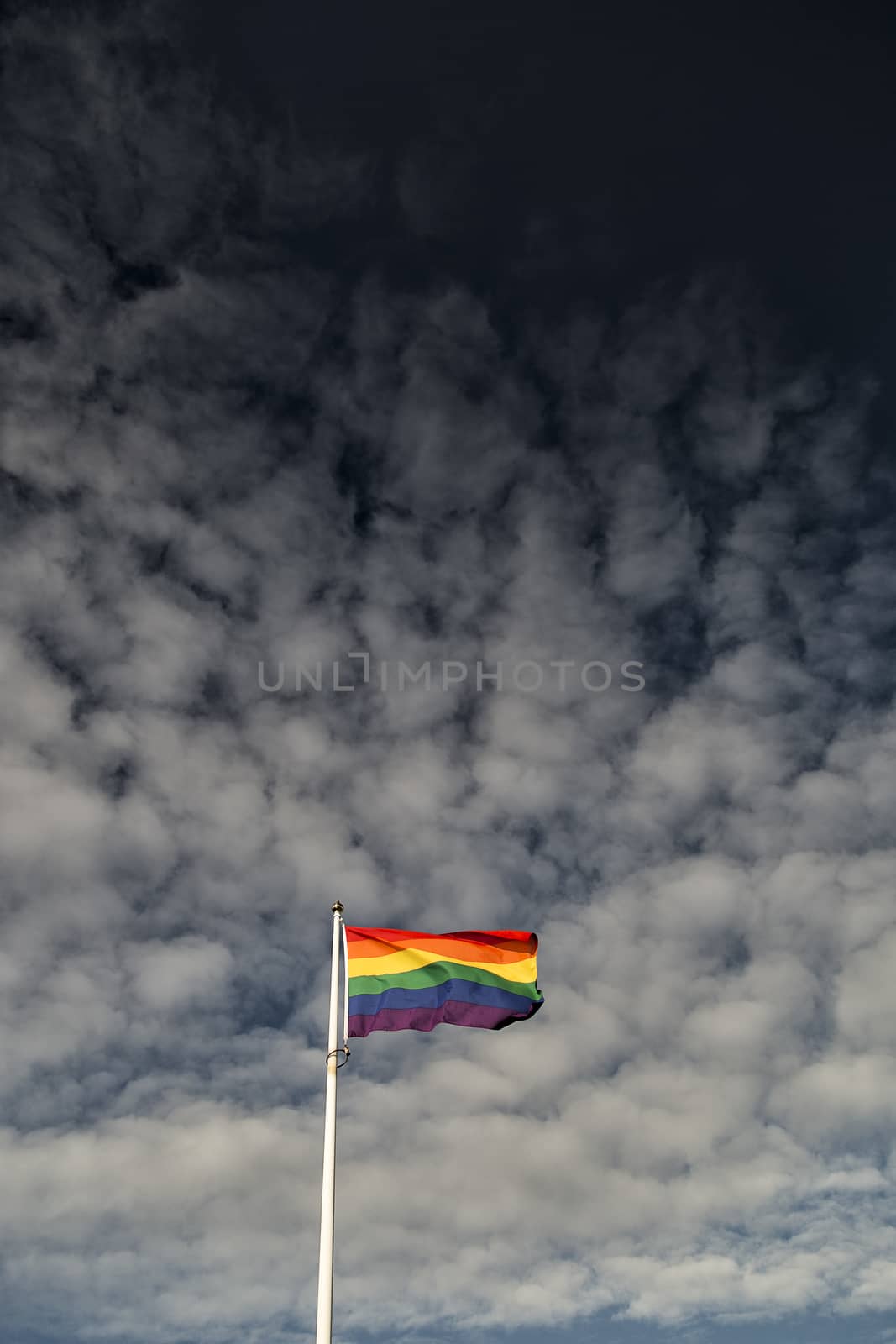 Rainbow Flag waving in the wind with a partly cloudy sky.