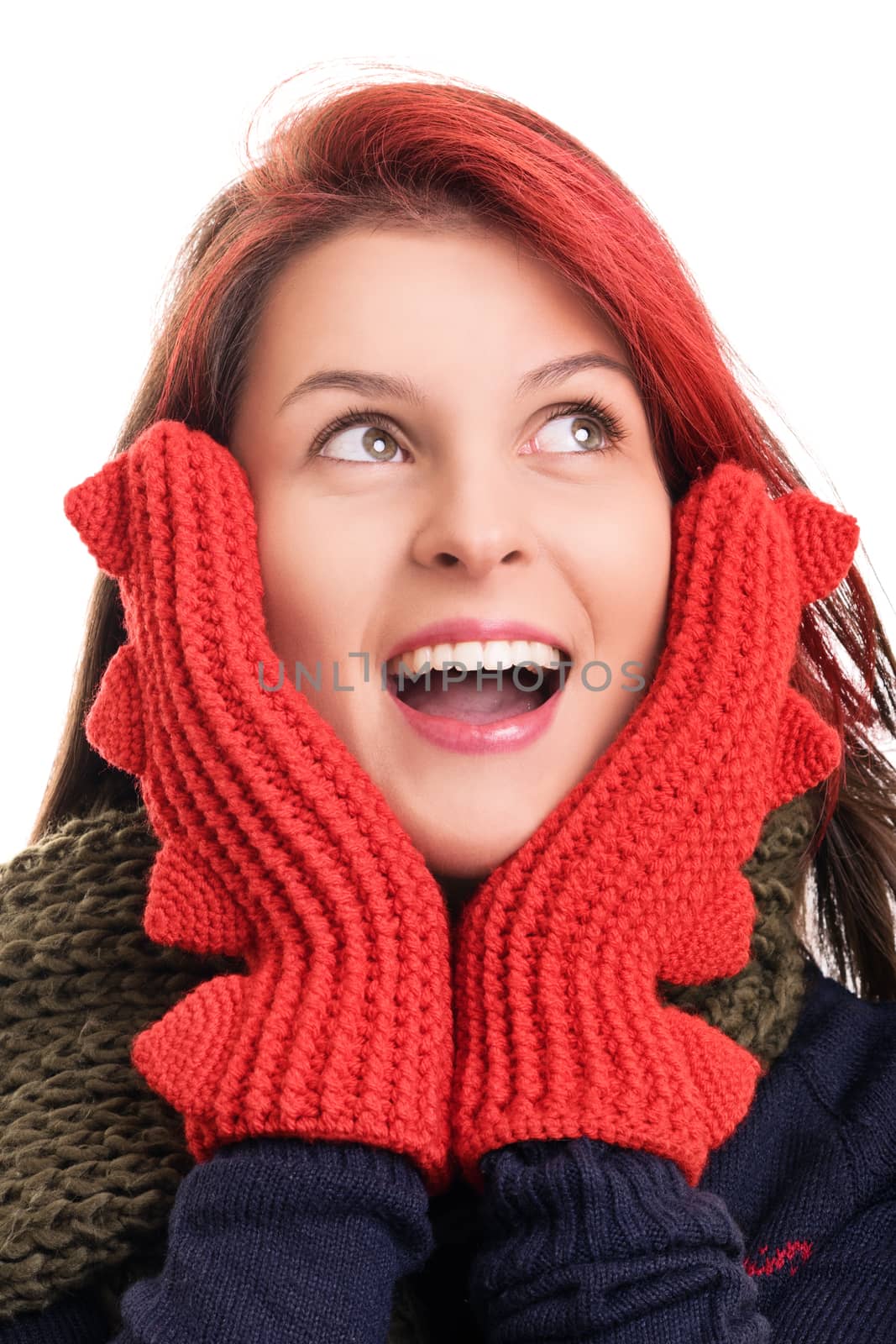 Close up shot of a beautiful surprised young woman with red mittens looking upwards, isolated on white background. Surprised young girl in winter clothes with open mouth holding her face, isolated on white background.