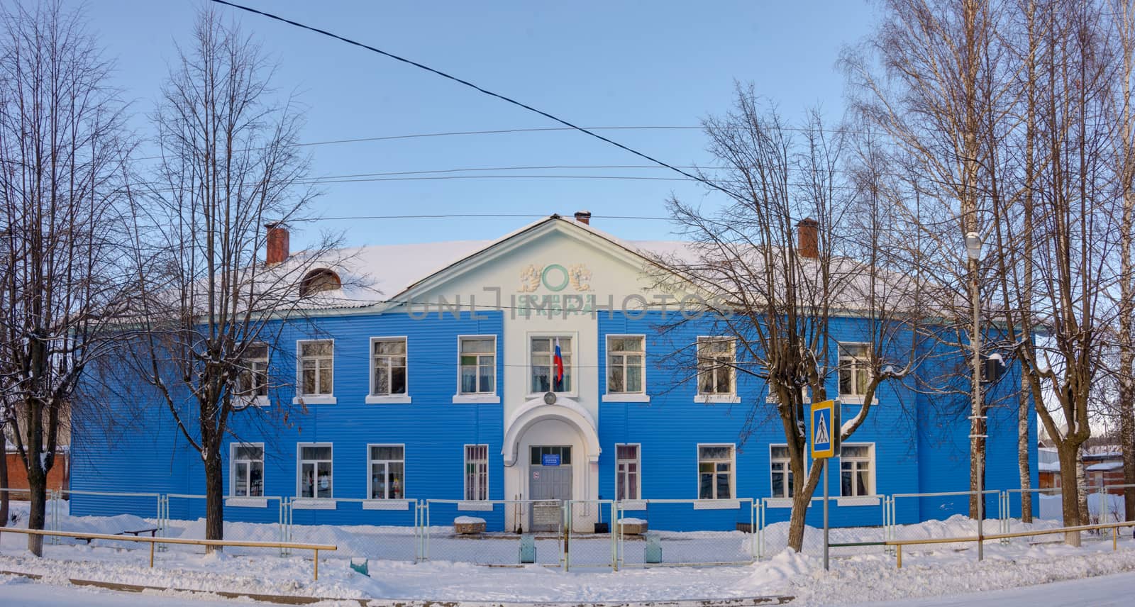A blue, two-story building on a snowy street, under a blue sky.