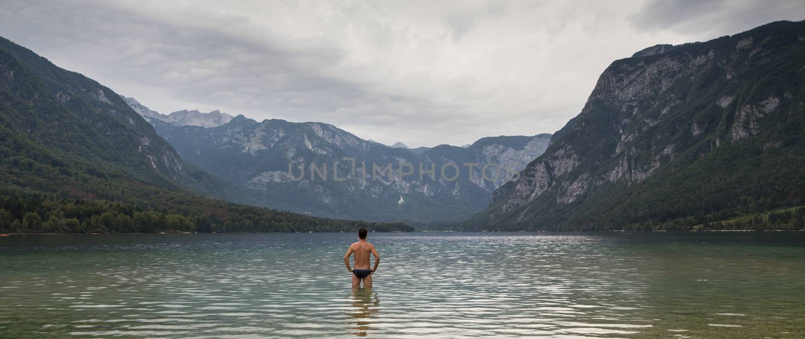 Man going to swim in freezing cold lake Bohinj, Alps mountains, Slovenia, on tranquil overcast morning by kasto