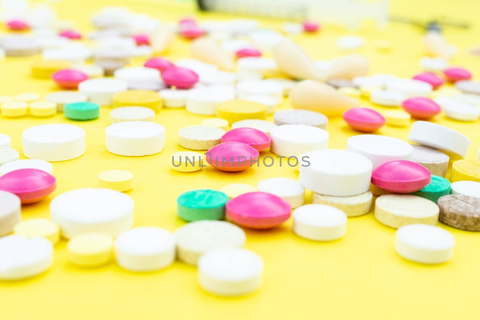Assorted pharmaceutical medicine pills, tablets and capsules over yellow background