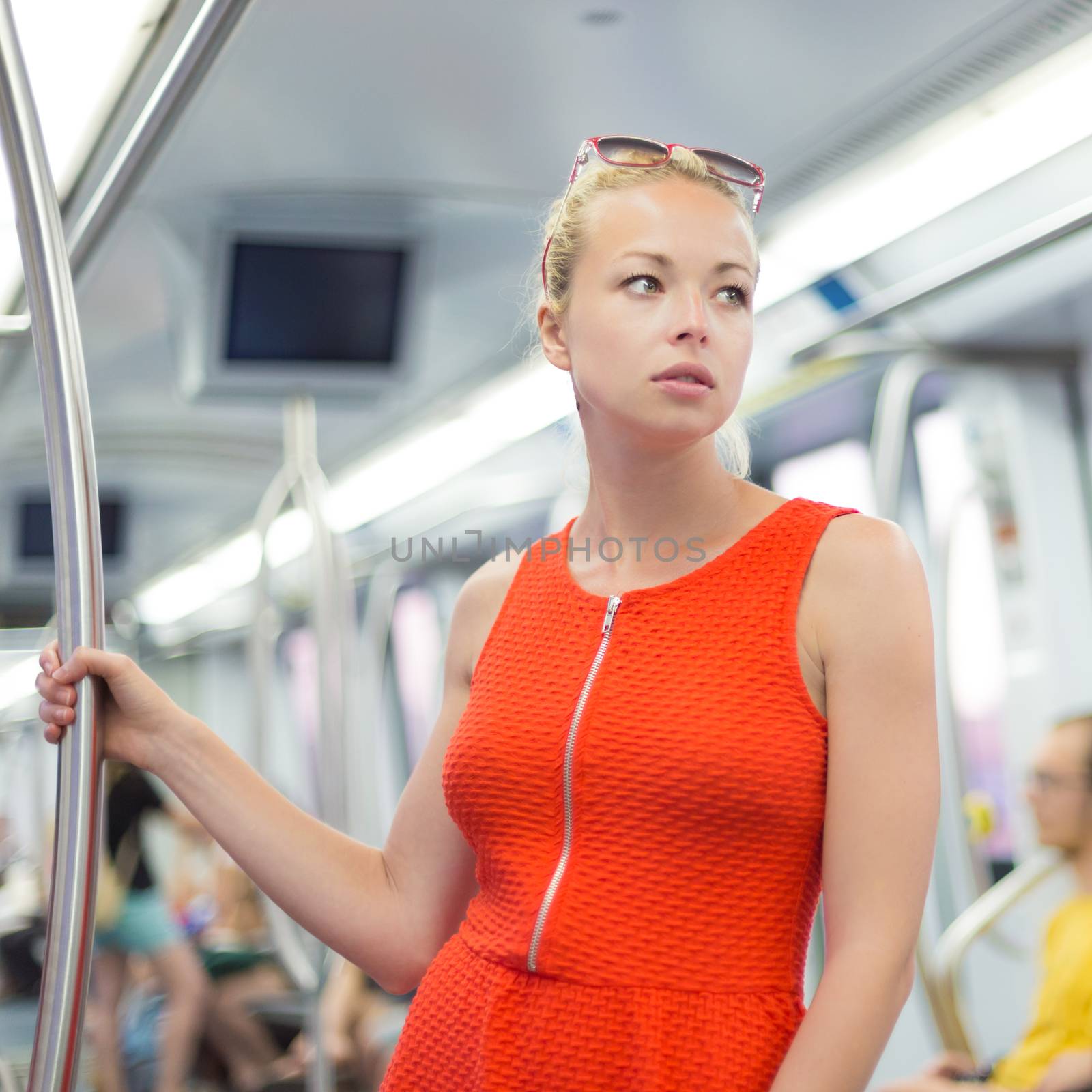 Beautiful blonde caucasian lady in red dress traveling by metro.