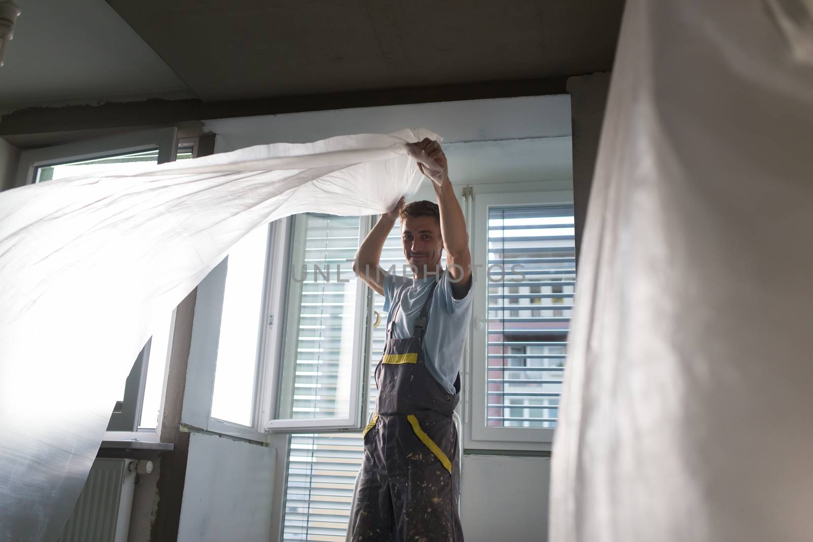 Construction worker wearing worker overall installing protective foil. House apartment renovation. Construction finishing works.