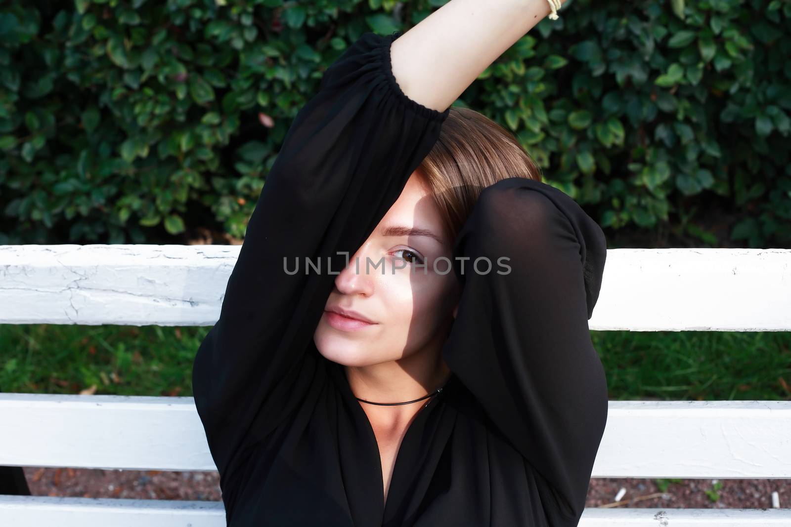 Beautiful young woman sitting on wooden bench in garden