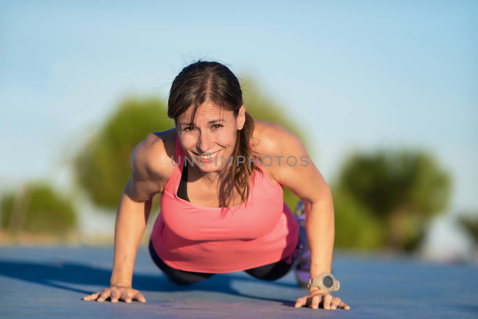 Fitness woman doing push-ups during outdoor cross training workout by HERRAEZ