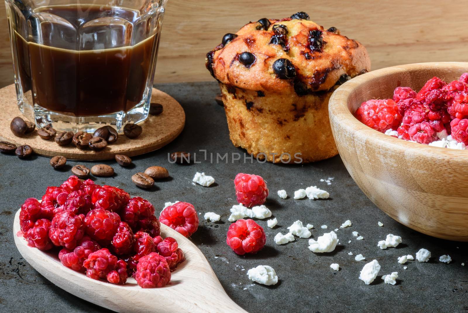 Cottage cheese with raspberries, coffee in a cup and blueberry muffin for breakfast with scattered berries, grains of curd and coffee beans