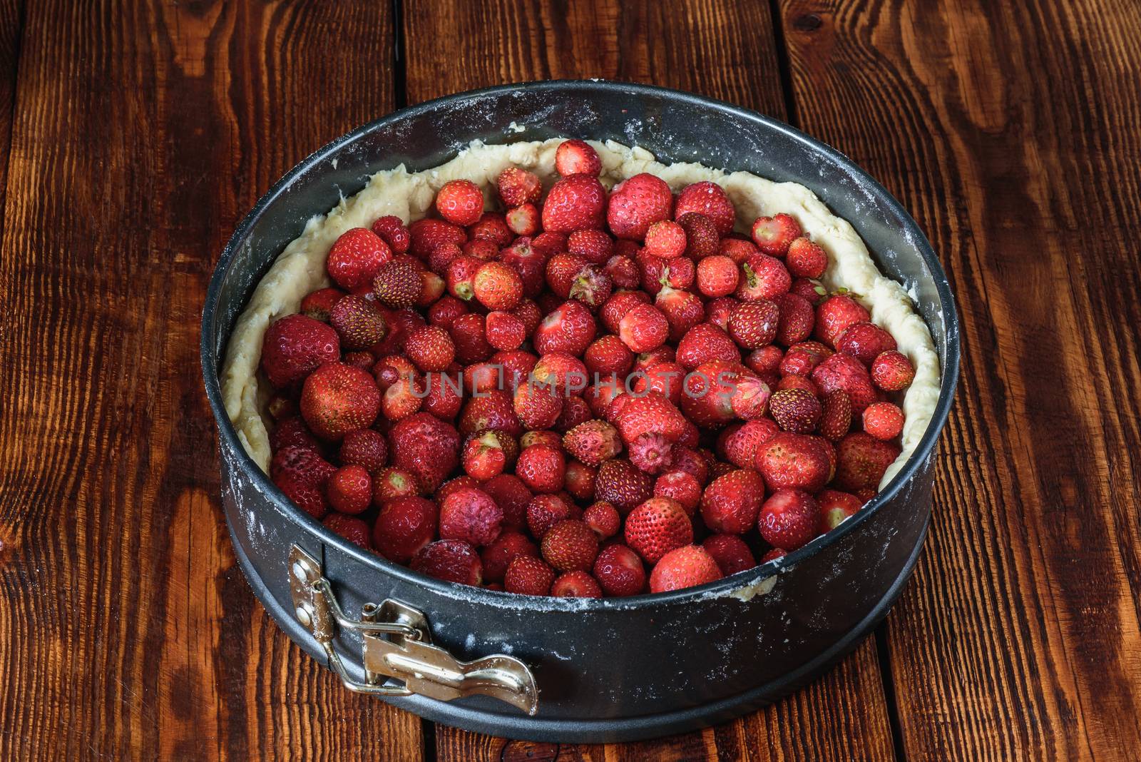 Cooking strawberry cake in metal baking dish on wooden table