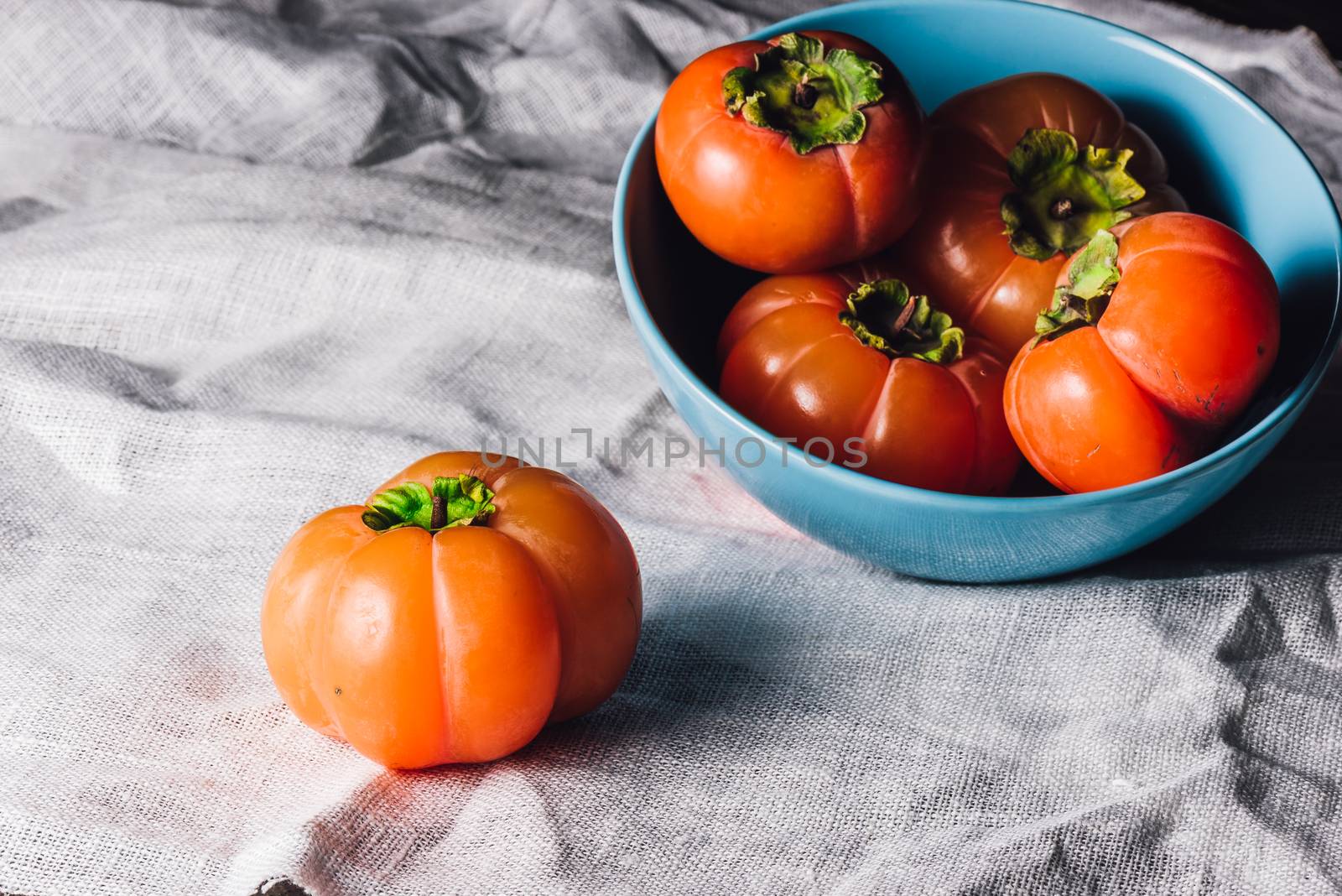 Ripe Persimmons in Blue Bowl Bowl ande One on Table