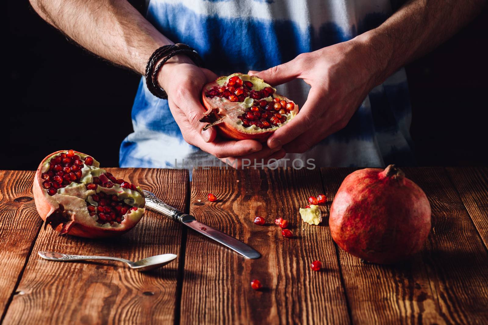Pomegranate Half in the Hands and Other Half on Wooden Table with Knife.