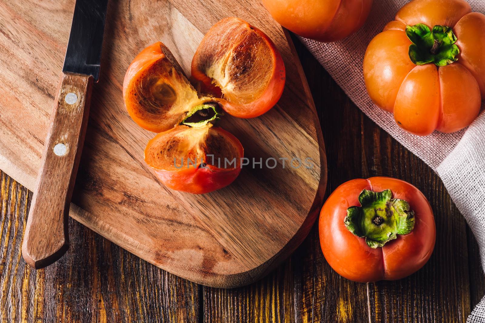 Persimmon Slices on Cutting Board with Kitchen Knife and Persimmons.