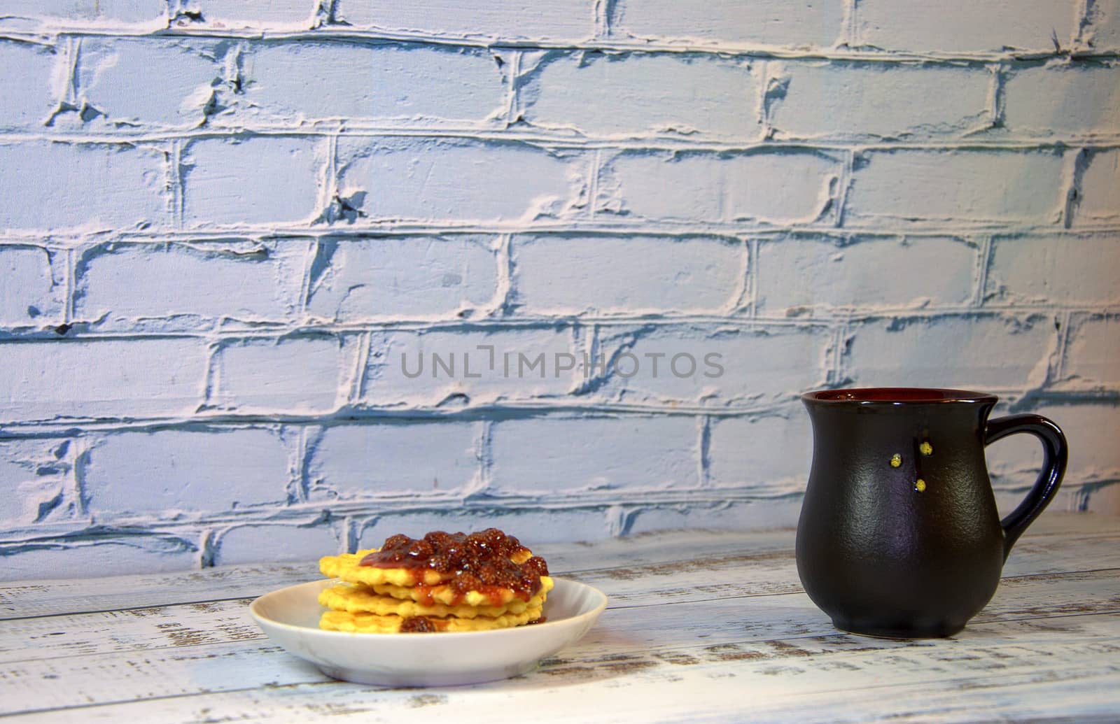 A mug of hot tea and a plate of waffles in strawberry jam. Close-up.