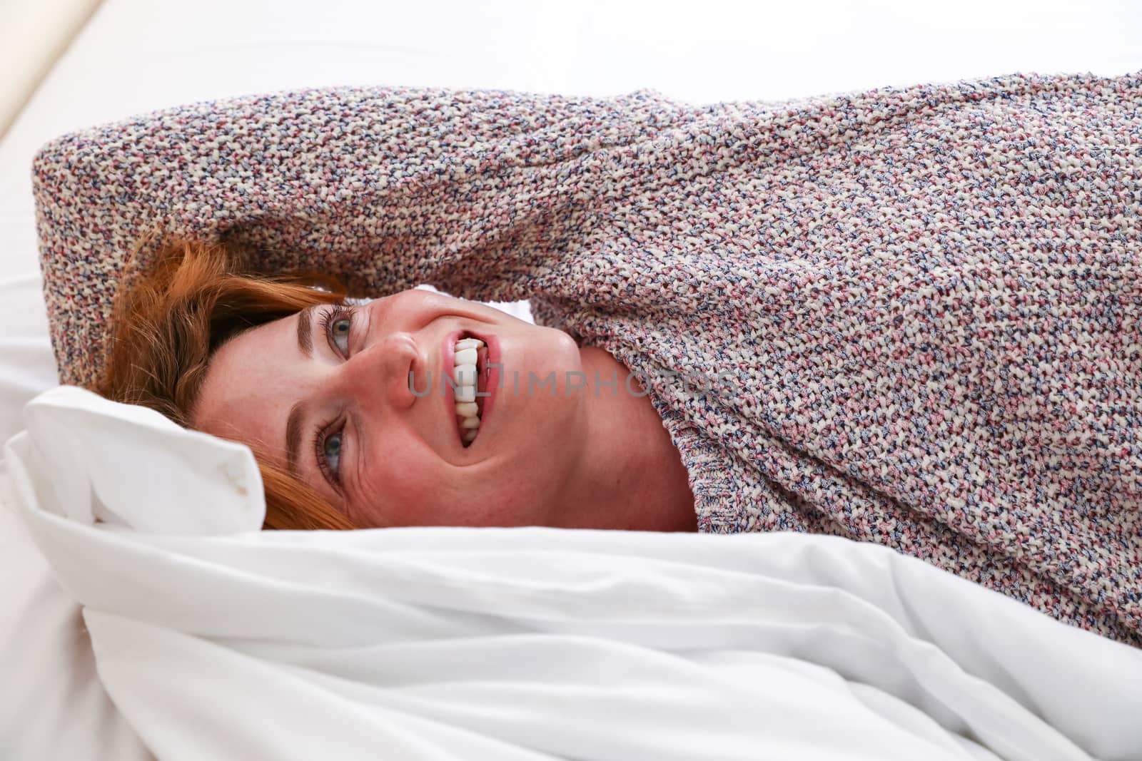 A beatiful woman lays down in her bed, smiling while waking up in the morning