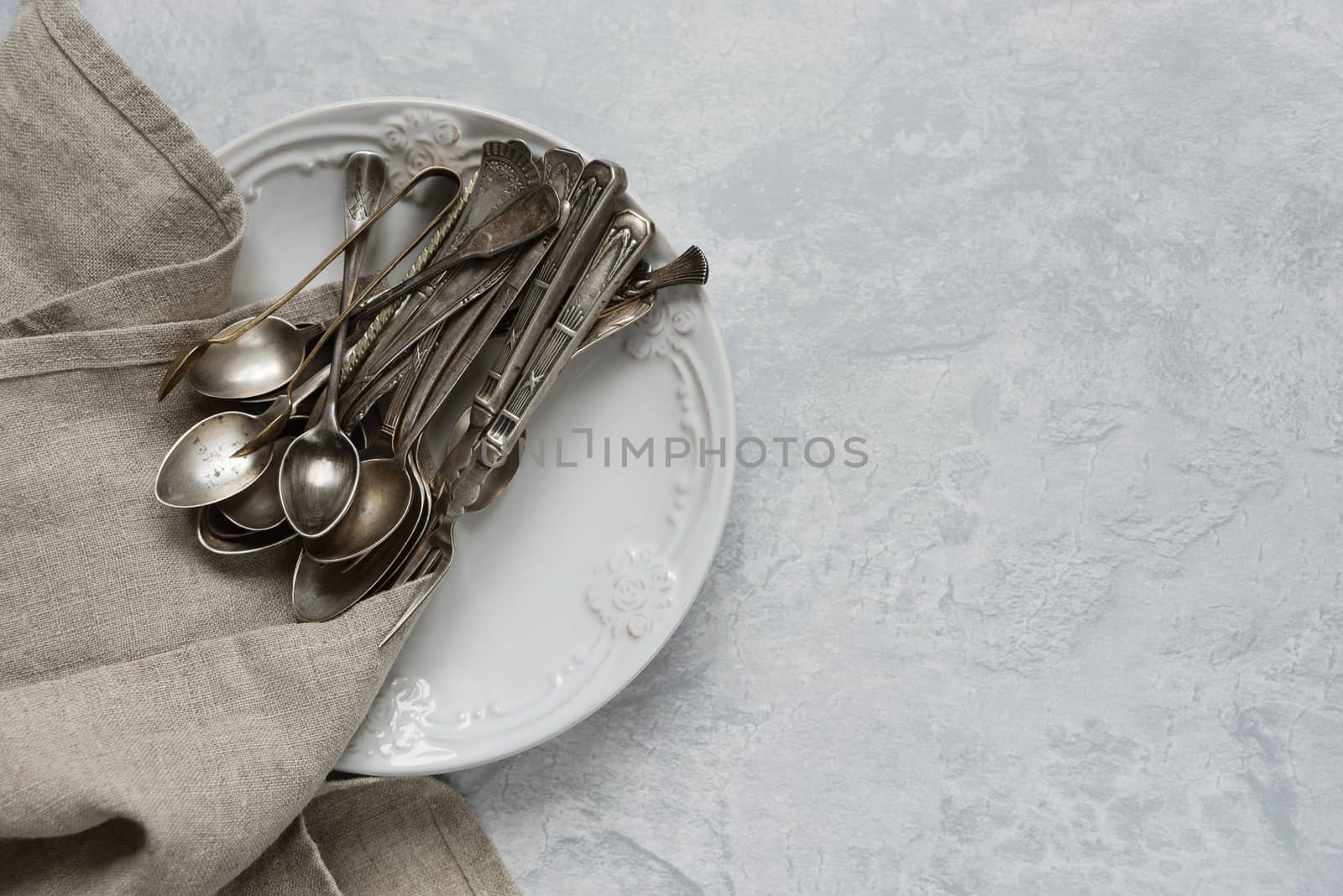 Various silverware on a ceramic plate on the background of gray concrete surface, with copy-space