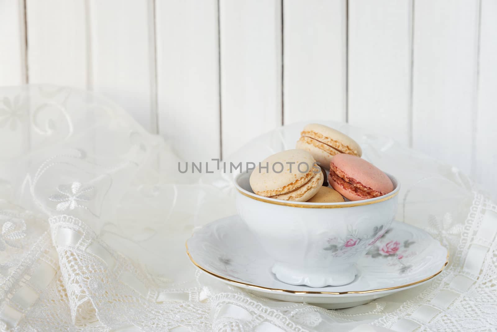 Beautiful elegant porcelain cup filled with almond cookies, on the background of white lace fabric