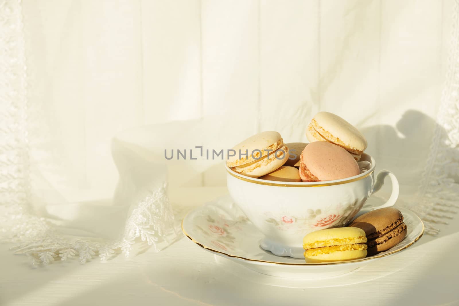 Beautiful elegant porcelain cup filled with almond cookies, on the background of white lace fabric